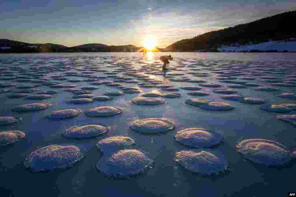 A skater observes pancakes snow on the frozen Lake des Rousses in Les Rousses, central-eastern France, Jan. 1, 2025. This phenomenon forms when slushy ice in water clumps into round, pancake-like shapes due to waves or currents.