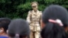 FILE - People stand in front of a statue of Gen. Aung San, late father of Myanmar National League for Democracy leader Aung San Suu Kyi, during a ceremony at a park in Yangon, Myanmar, July 19, 2015. 