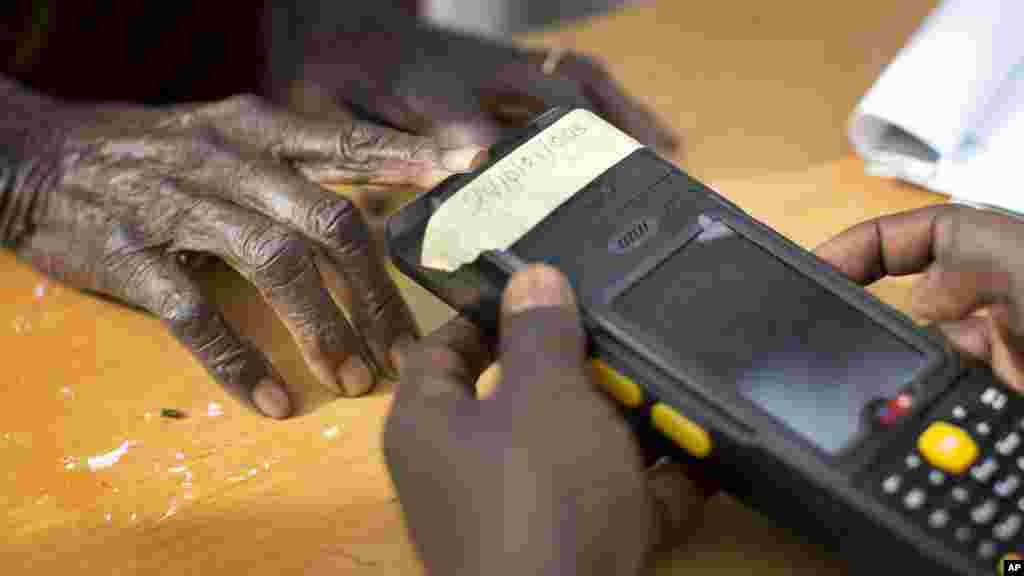 Une vieille femme nigériane fait valider sa carte de vote à travers un lecteur d'empreintes digitales, avant de revenir voter plus tard dans la journée, dans la ville natale du candidat de l'opposition le général Muhammadu Buhari, en Daura, Nigeria samedi 28 mars 2015.